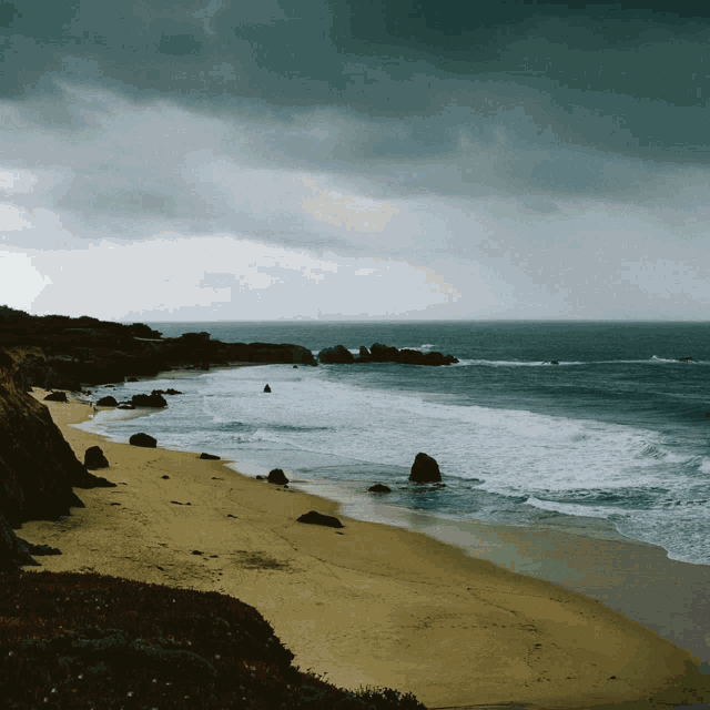 a beach on a cloudy day with waves crashing on the sand