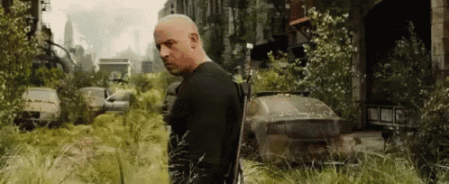 a man in a black shirt is standing in a field with a gun .