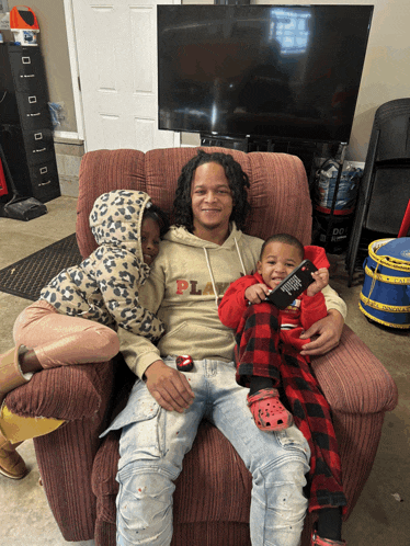 a man is sitting in a chair with two children and a remote control