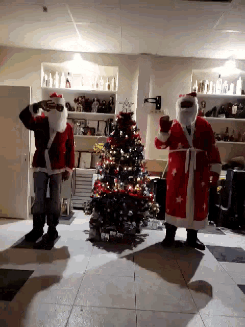 two men dressed as santa claus standing next to a christmas tree