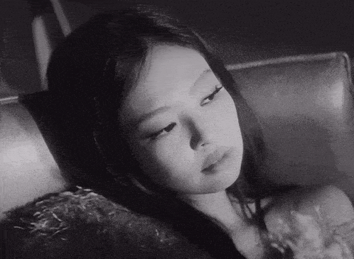 a black and white photo of a young woman laying down on a couch .