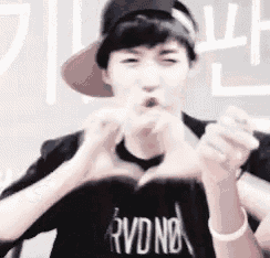 a man wearing a hat and a black shirt is making a heart with his hands .