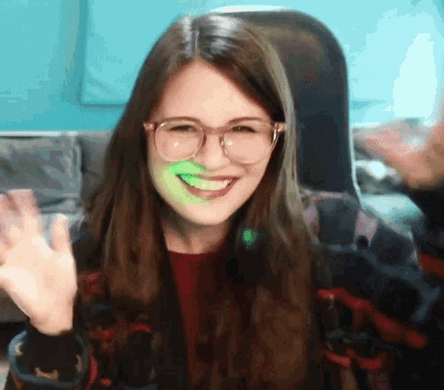 a young woman wearing glasses is smiling and waving