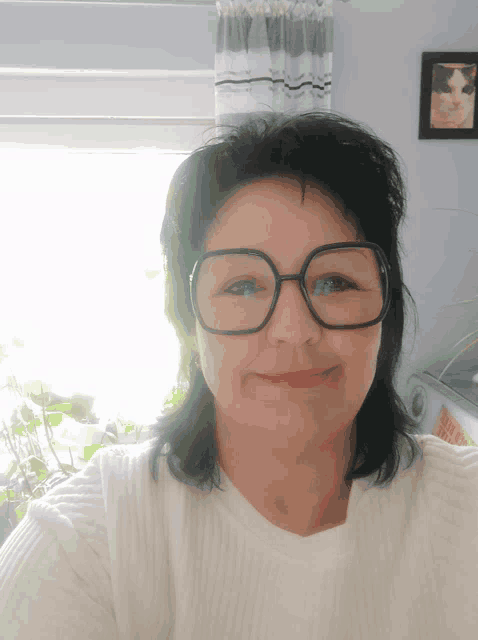 a woman wearing glasses and a white sweater smiles for the camera