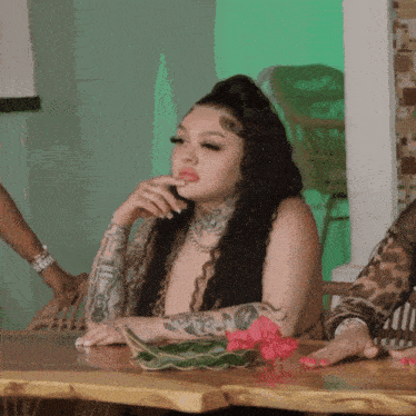 a woman with tattoos on her arm sits at a table with a flower in front of her