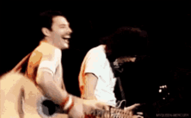 two men are playing guitars on a stage and singing .