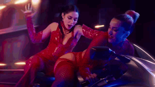 two women are sitting on a motorcycle in a dark room