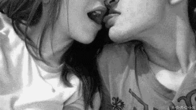 a black and white photo of a man and woman kissing on a bed .