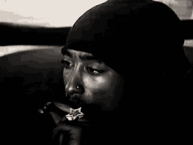 a man in a black hat is smoking a cigarette in a black and white photo .