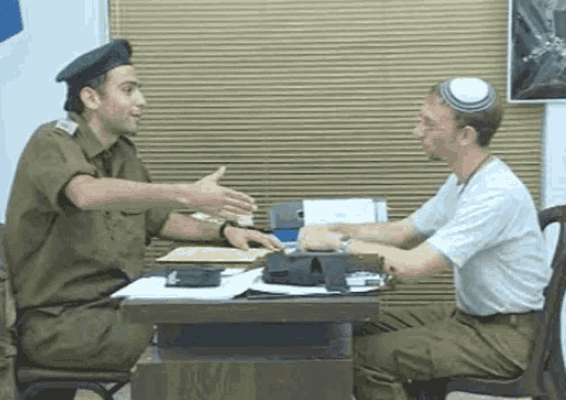 two men in military uniforms are sitting at a table talking to each other