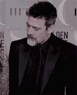 a man with a beard is wearing a tuxedo and a black shirt .