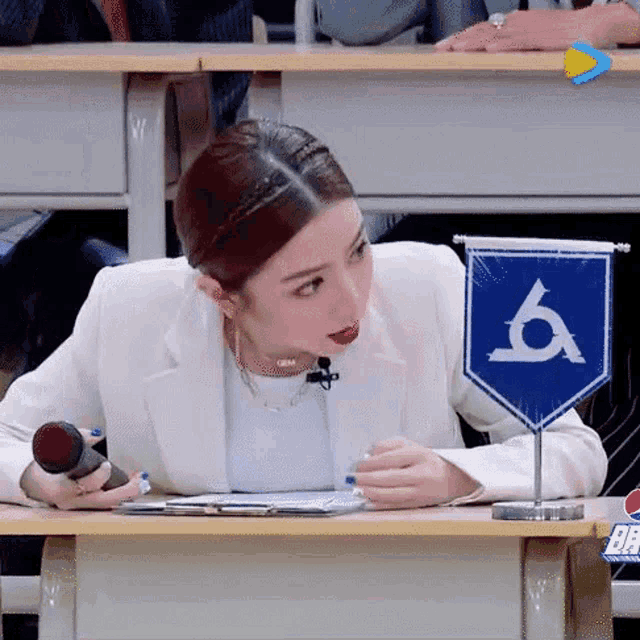 a woman in a white suit is sitting at a desk with a microphone and a blue flag .
