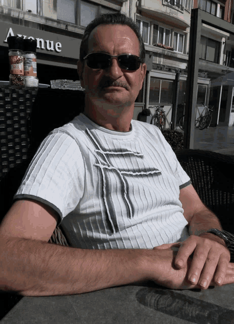 a man wearing sunglasses sits at a table in front of avenue