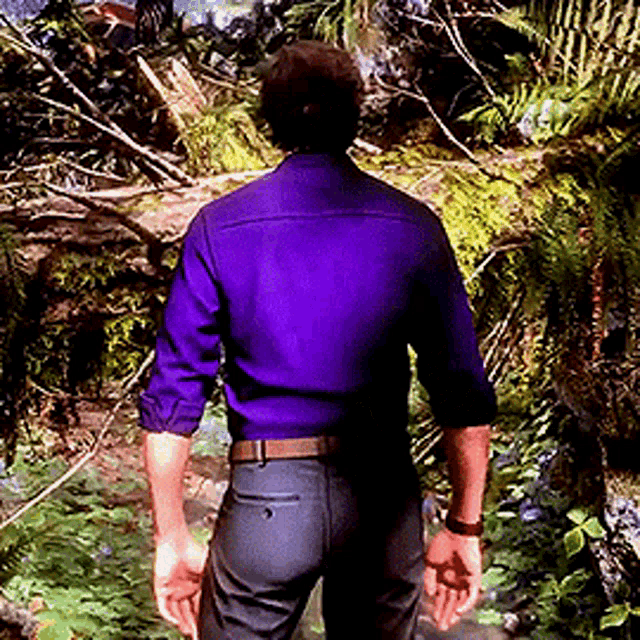 a man in a purple shirt and black pants stands in the woods