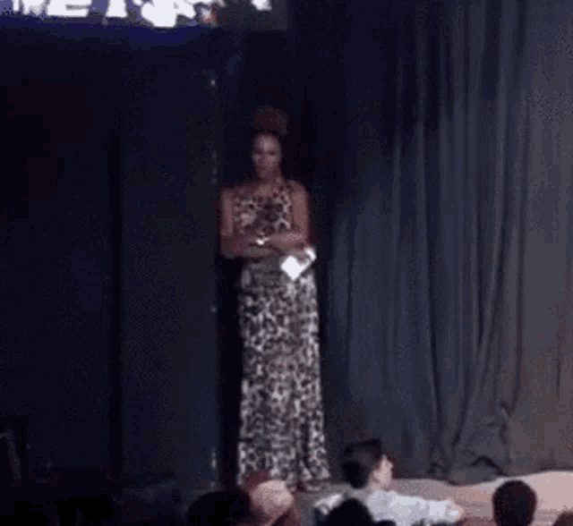 a woman in a white dress stands on a stage in front of a crowd