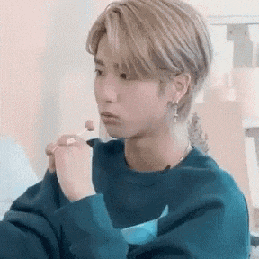 a young man wearing a blue sweater and earrings is eating a sandwich .
