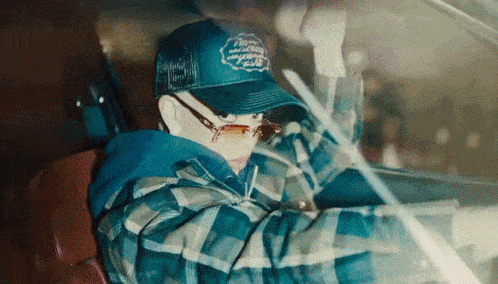 a person wearing a blue trucker hat and sunglasses driving a car