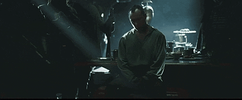 a man is sitting in a dark room with his hands folded
