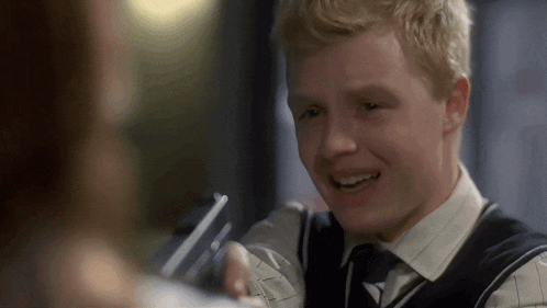 a young man in a vest and tie smiles while talking to a woman