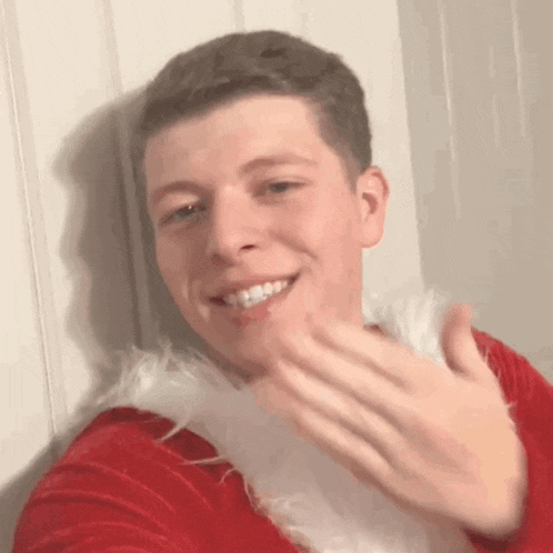 a young man wearing a santa claus costume is smiling and waving at the camera .