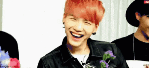 a young man with red hair is laughing while holding flowers in his hands .