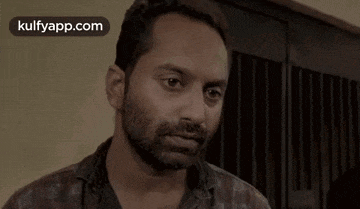 a man with a beard is looking at the camera while wearing a plaid shirt .