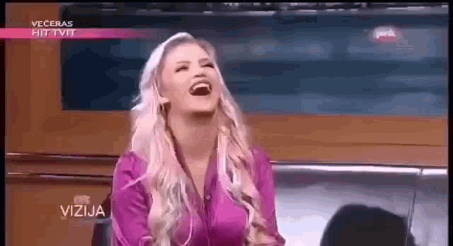 a woman in a pink shirt is laughing on a television show