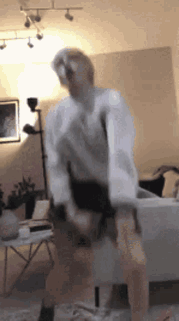 a woman is dancing in a living room in front of a couch and a lamp .
