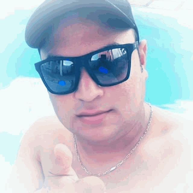 a shirtless man wearing sunglasses and a baseball cap is giving a thumbs up