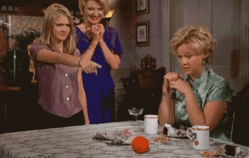 three women are sitting at a table and one is pointing at something