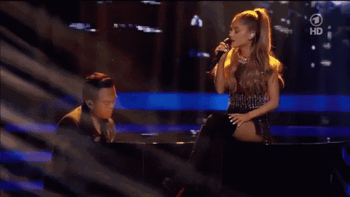 a woman singing into a microphone while a man plays a piano in front of a screen that says hd on it