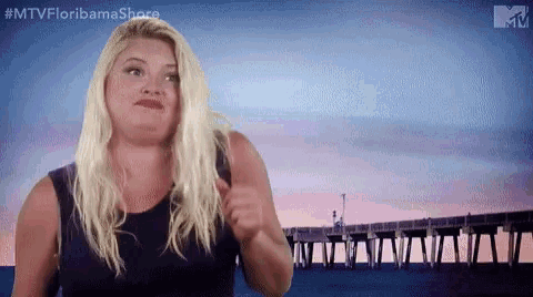 a blonde woman is standing in front of a pier and making a funny face .