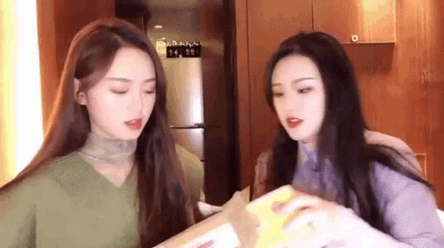 two women are standing next to each other in a kitchen and looking at something .