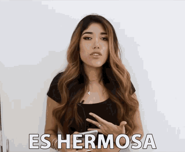 a woman holds a cell phone in front of a sign that says es hermosa on it