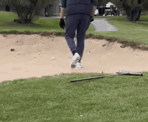 a man is walking on a golf course with a rake in the grass .