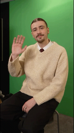 a man in a sweater and tie is waving his hand
