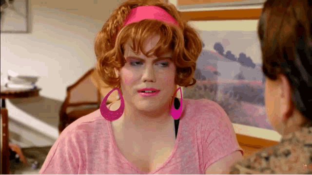 a woman wearing pink earrings and a pink headband is talking to another woman