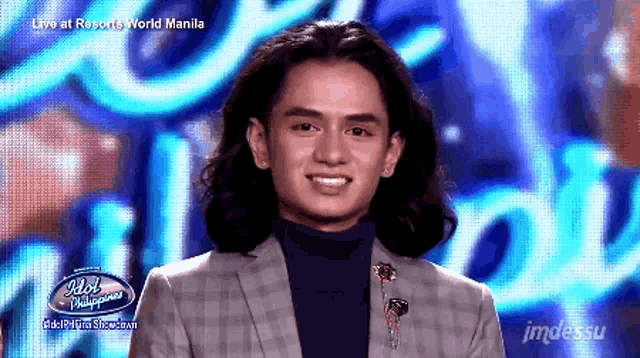 a man with long hair is smiling in front of a screen that says idol philippines on it