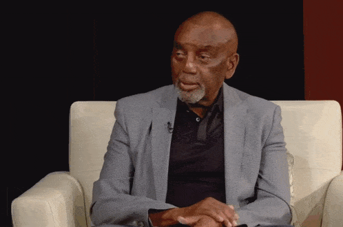 a man in a suit and black shirt sits in a chair