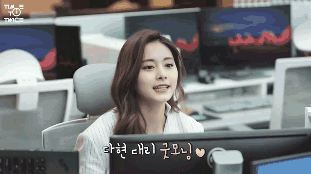a woman sitting in front of a computer with a twice logo on the bottom right