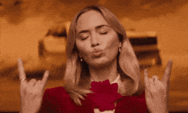 a woman in a red jacket is making a devil horns sign with her hands