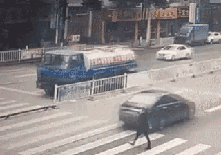 a man is crossing the street while a car is driving by .