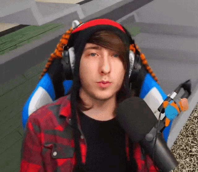 a man wearing headphones and a plaid shirt is sitting in a chair talking into a microphone