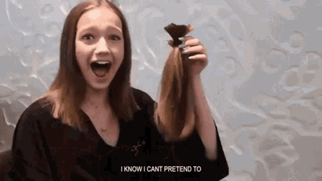a young girl is holding a piece of hair in her hand and says `` i know i can t pretend to '' .