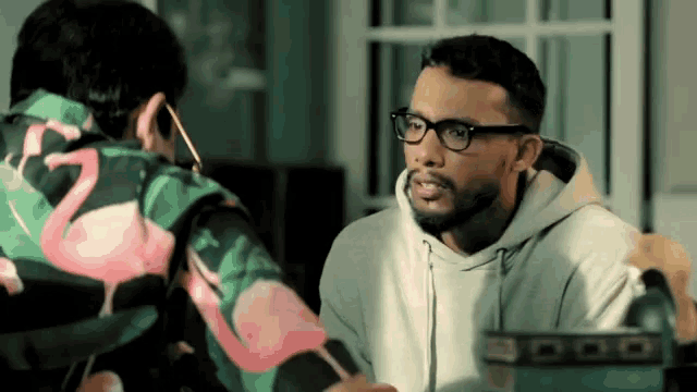 a man wearing glasses talks to another man wearing a flamingo jacket