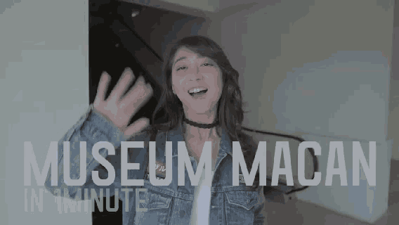 a woman is standing in front of a sign that says museum macan in 1 minute