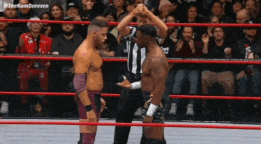 two wrestlers are shaking hands in a ring with a referee .