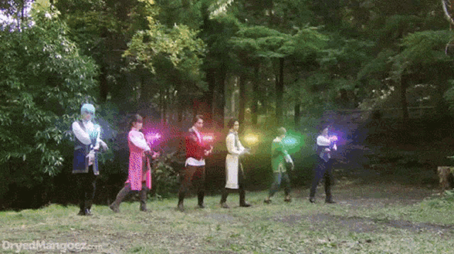 a group of people are standing in a line in the woods holding glowing objects in their hands .