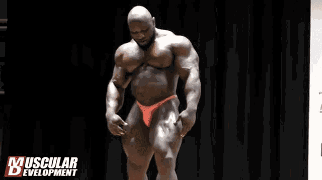 a muscular man in a red bikini flexes his muscles on a stage