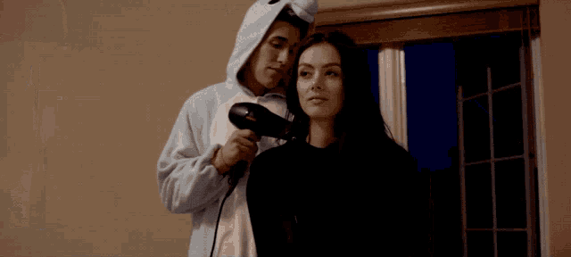 a woman is getting her hair blow dried by a man in a unicorn hoodie